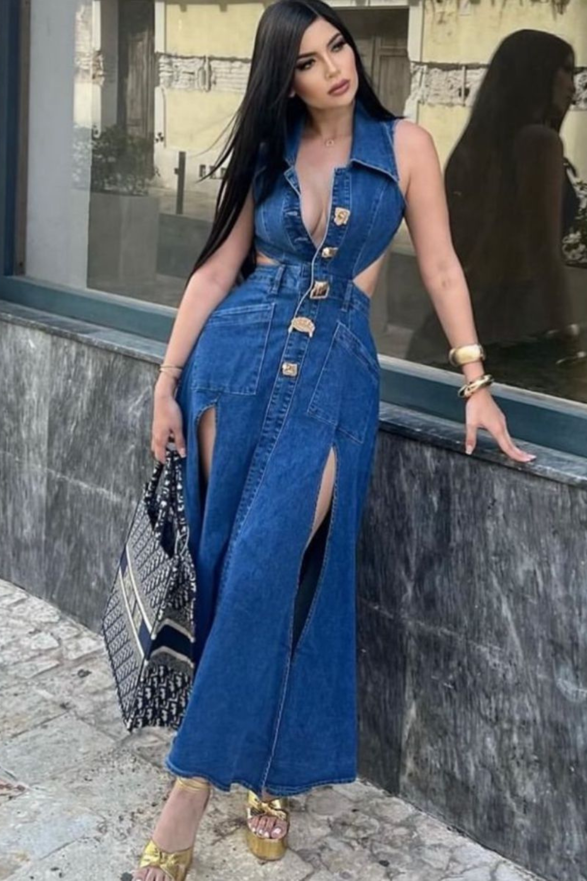 button-up denim maxi dress with side slits, accessorized with gold heels, bracelets, and a patterned handbag.